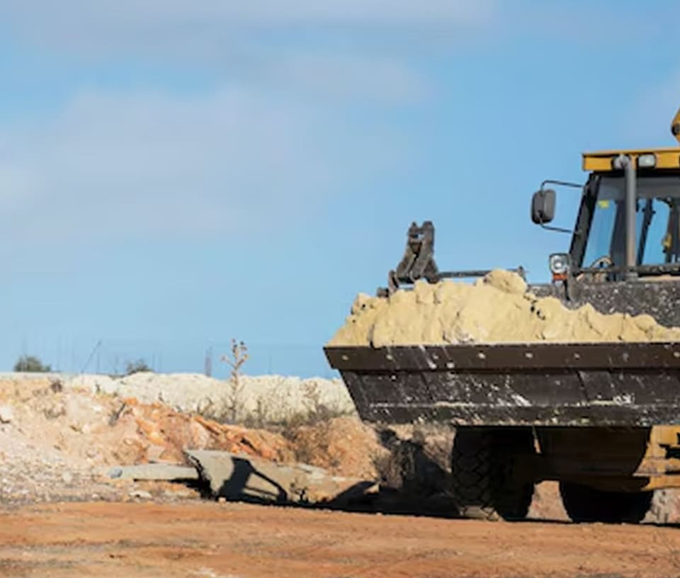 Wheel loader carrying a bucket of sand at the extraction site under a clear sky